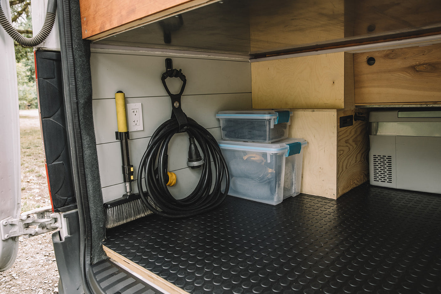RV rental storage: Organized rear cargo area with shore power cord, broom, cooler, and clear bins.