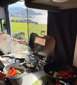 Cooking a meal in an RV rental with a stunning ocean view, horses grazing, and rice steaming on the stove.