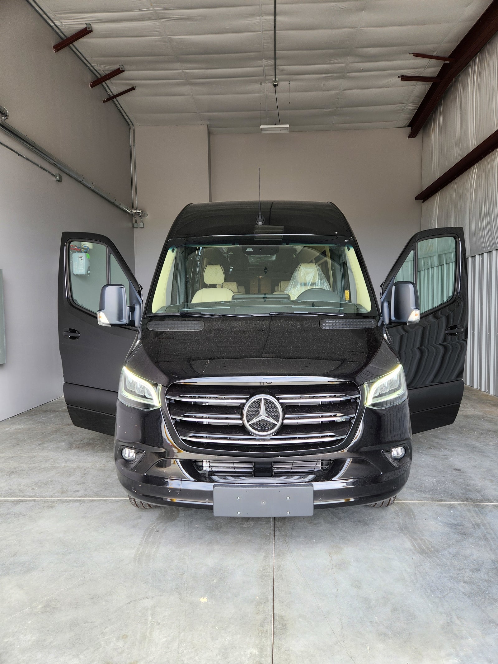 Discover this new black Mercedes-Benz Sprinter van, perfect for rv rental. Front doors open, showcasing a luxurious interior.