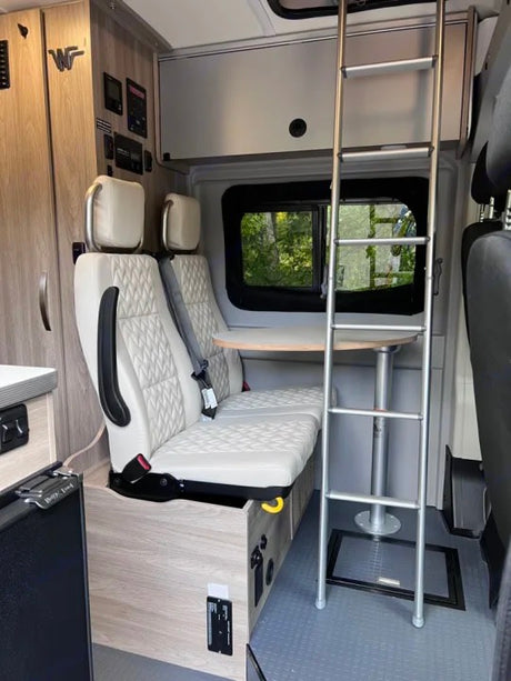 An RV rental's interior features a compact dinette with light seating, a table, and a ladder to an upper bunk.