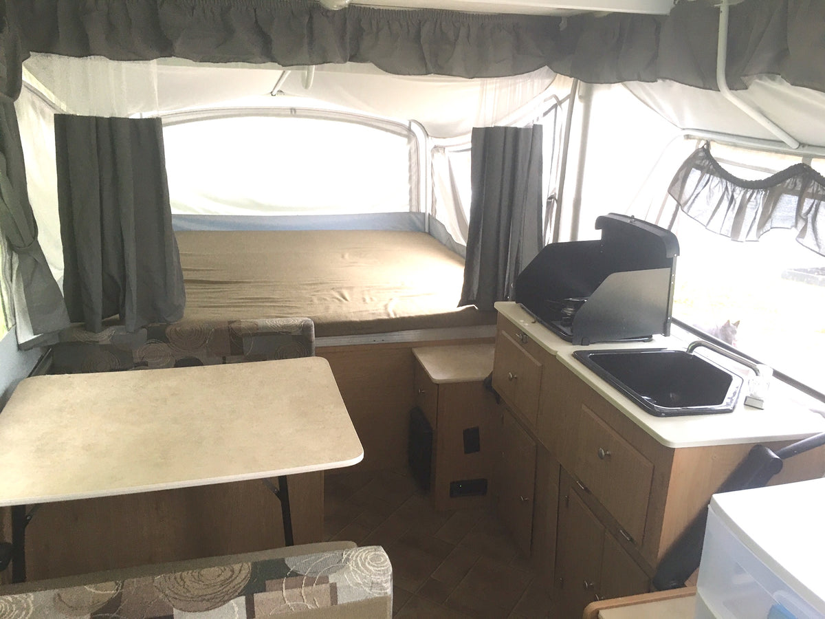 Bright pop-up camper interior, ideal for RV rental. Features bed, dining, & compact kitchen with stove & sink. — photo 5