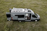 Explore the outdoors with this grey camper van RV rental, featuring solar panels and open doors revealing its cozy interior in a grassy field.