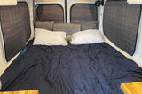Cozy RV rental bed in a camper van interior, featuring dark bedding, white pillows, and insulated windows.