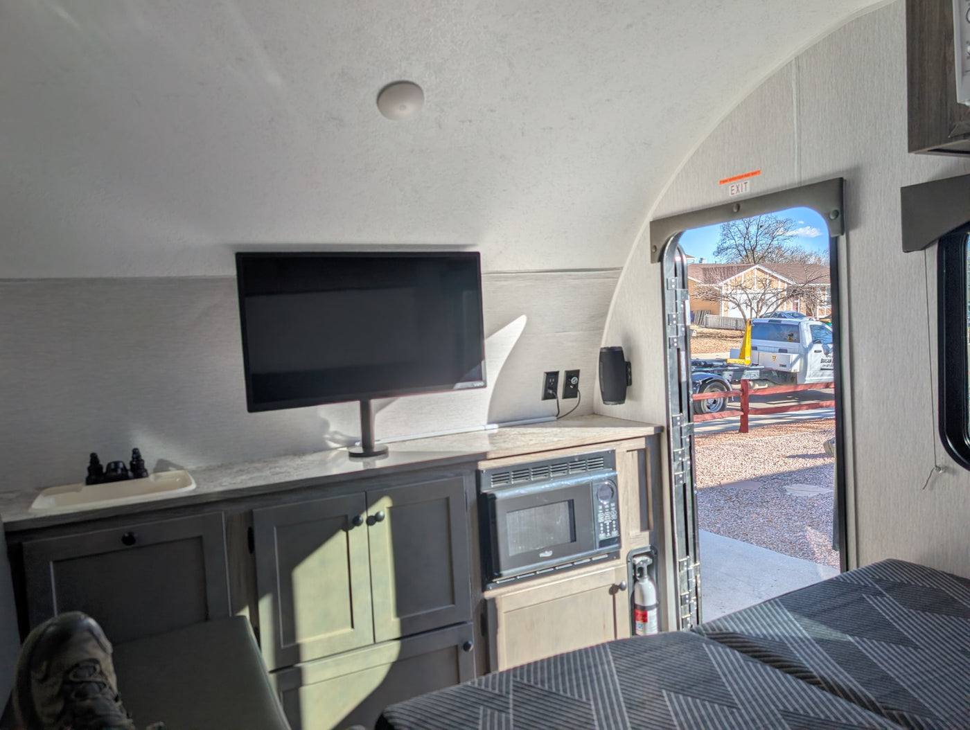 Cozy RV rental interior with a TV, microwave, and bed. The open door offers a glimpse of the outside world. — photo 13