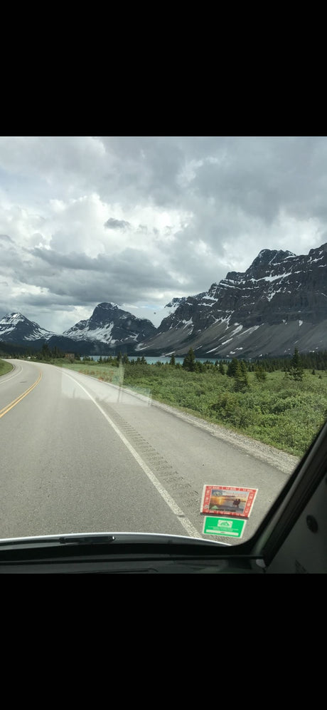 Scenic RV rental drive through Canadian Rockies, featuring snow-capped mountains, winding road, and turquoise lake.
