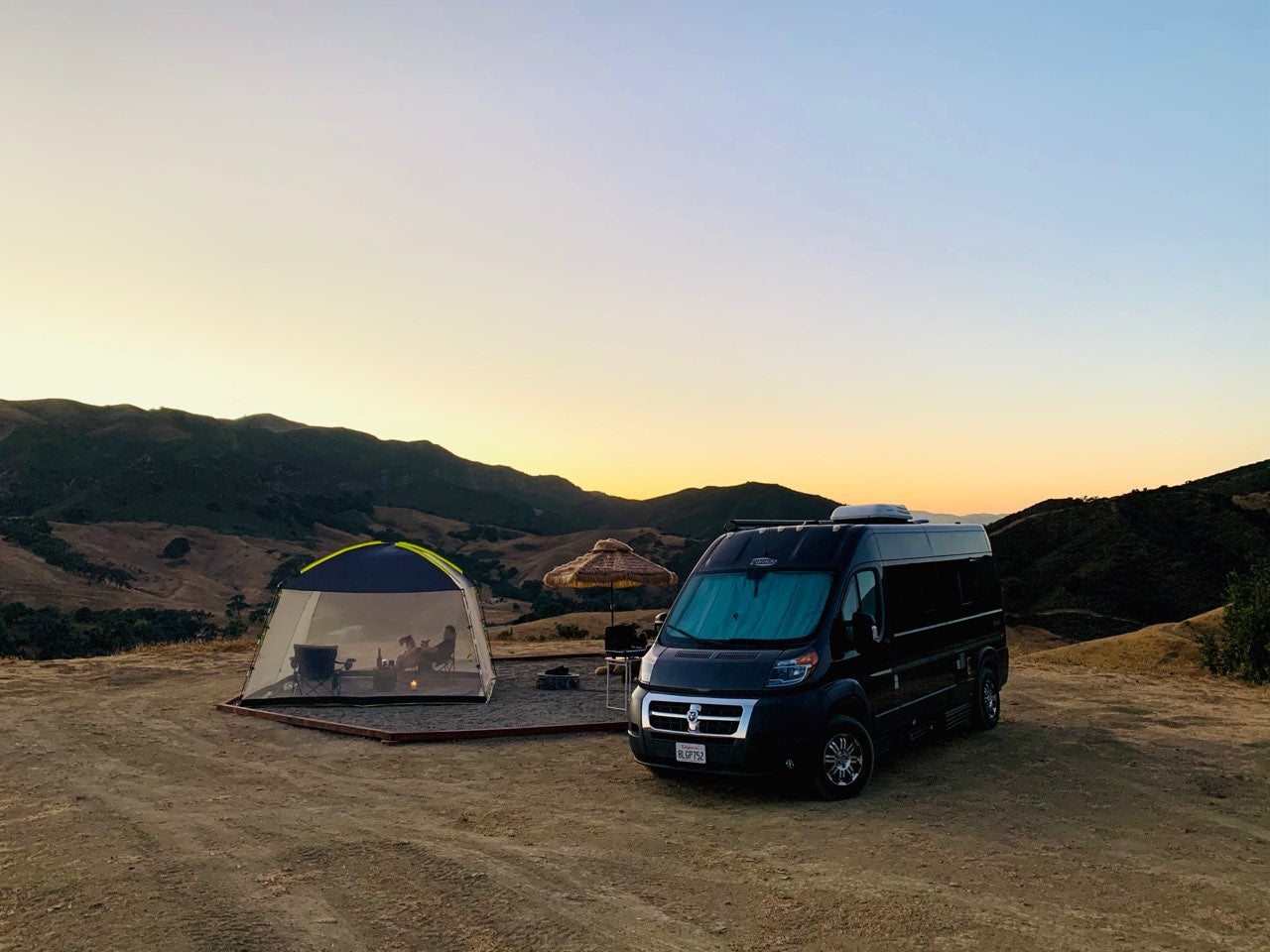  set up at a scenic mountain camp during sunset.|An RV rental's cozy bed features red linens — photo 1