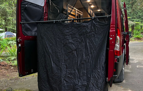 A red RV rental van with its rear doors open, featuring a black privacy screen for outdoor changing or showering at a campsite.