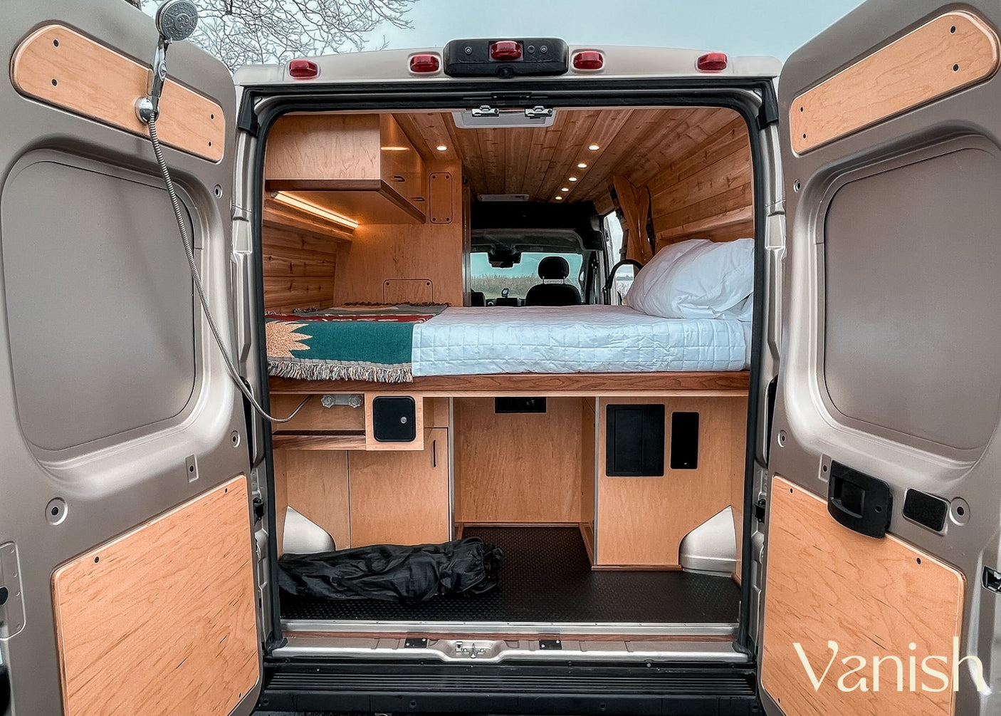 RV rental: rear view of wood-paneled interior, bed, storage, and outdoor shower hookup, ready for adventure.