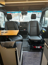 RV rental van interior: Driver & passenger seats, dashboard, custom table with cup holders, and a fire extinguisher.