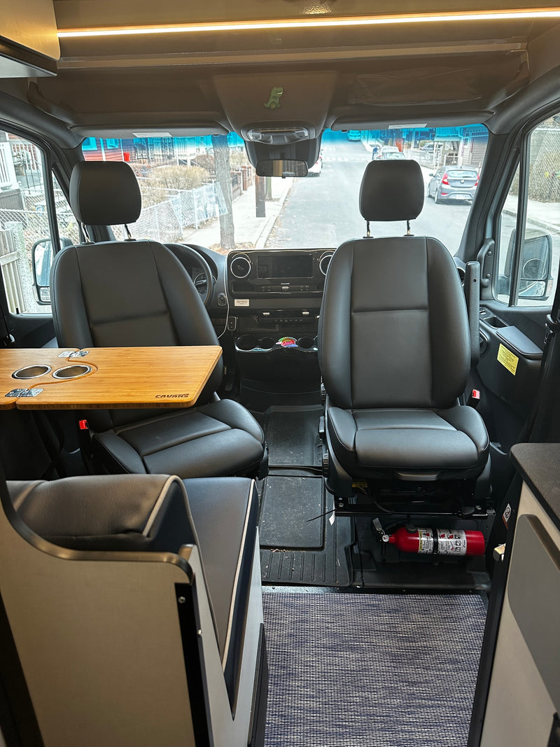 RV rental van interior: Driver & passenger seats, dashboard, custom table with cup holders, and a fire extinguisher. — photo 9