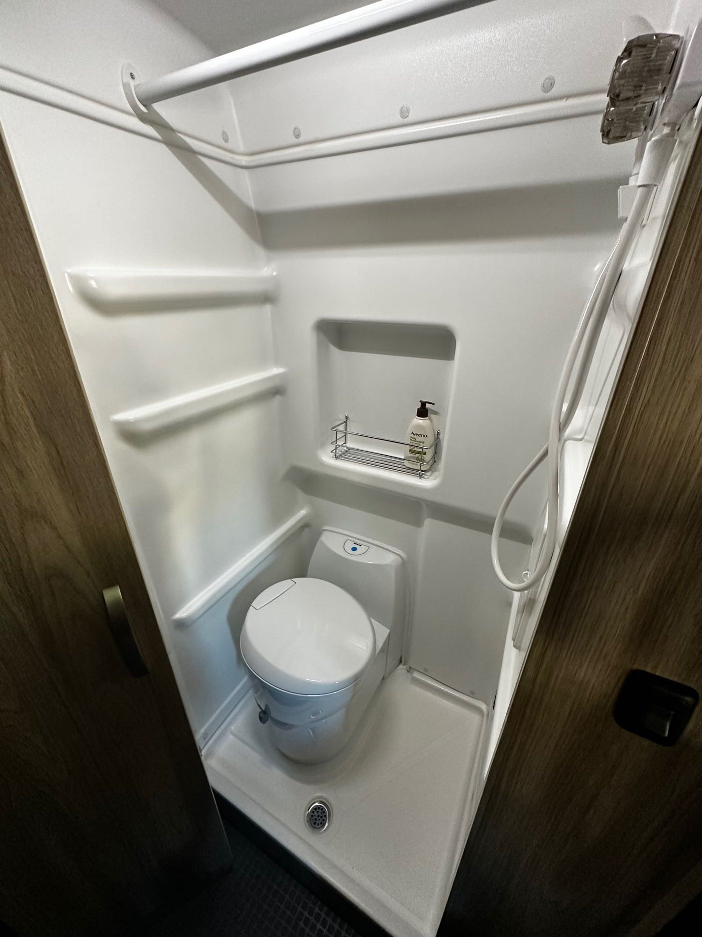 Compact RV rental wet bath with integrated toilet, shower, shelves, and a drying rod above.