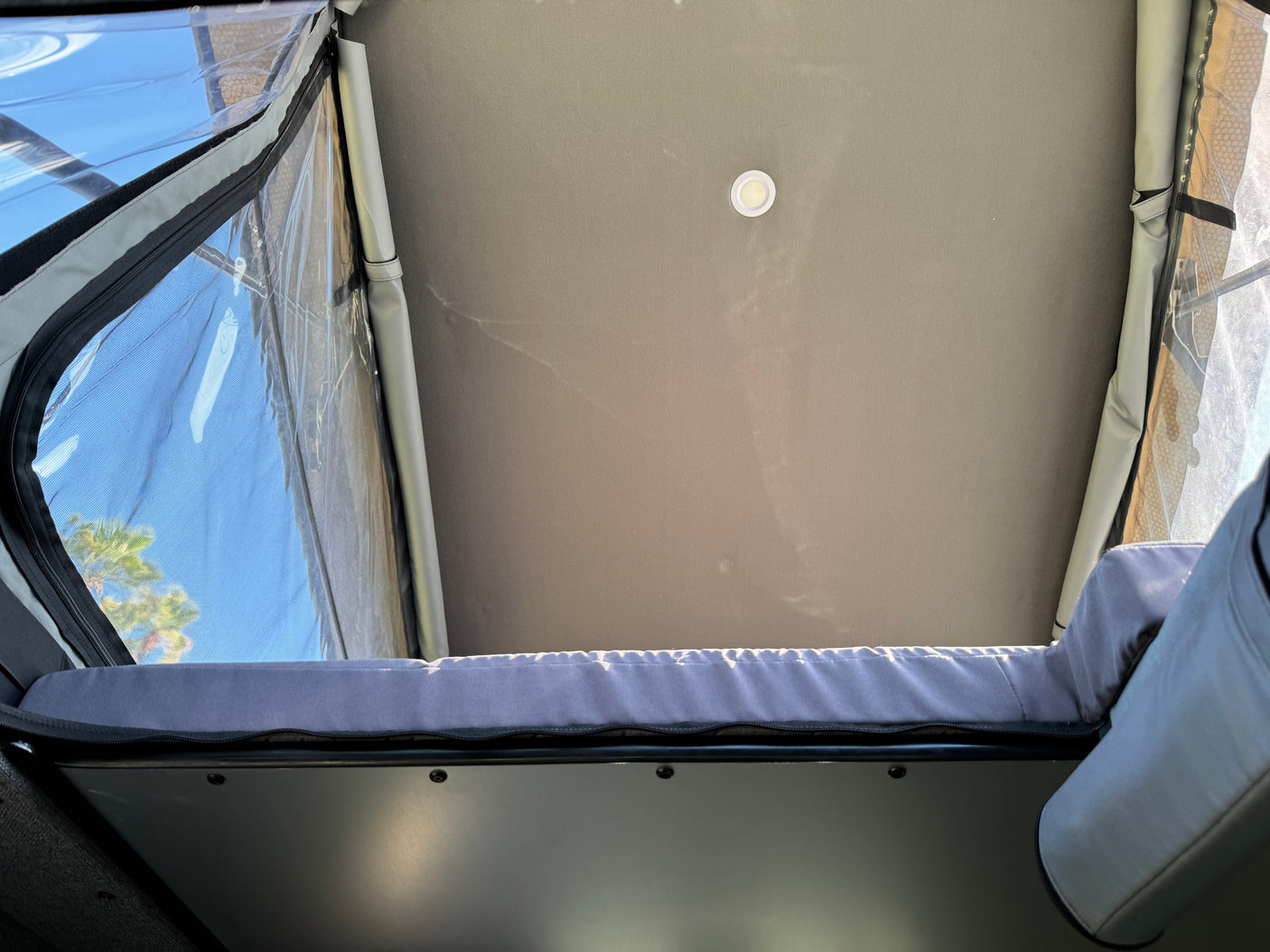 RV rental interior: Looking up into a pop-top tent, showing a comfortable bed, ceiling light, and clear window with sky view.