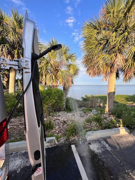 Enjoy an RV rental with an outdoor shower setup, perfect for washing off by the beautiful coastal waters. Palm trees line the view.