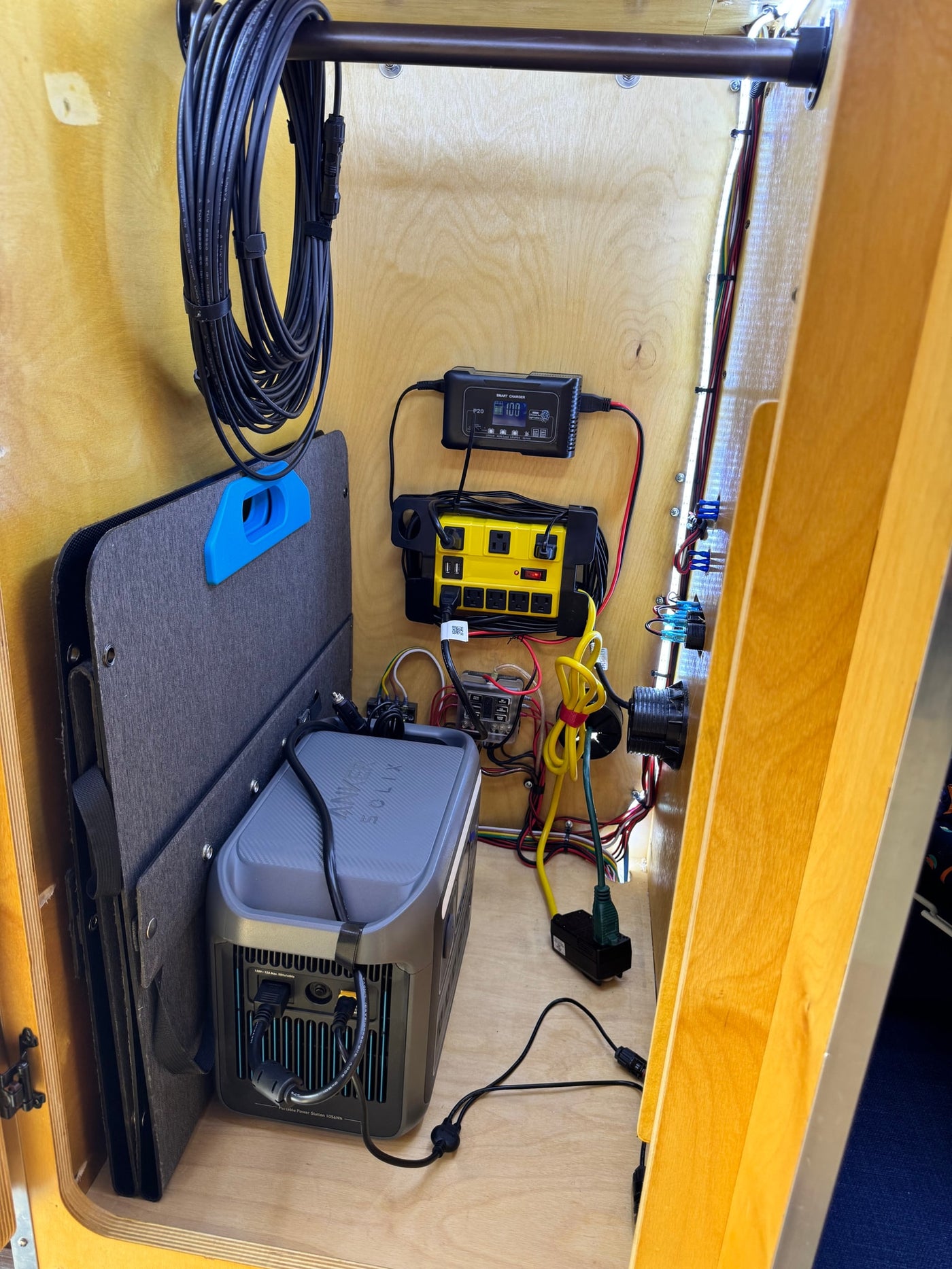 RV rental power setup in a wood cabinet, featuring an Anker Solix power station, smart charger, and stored solar panel. — photo 7