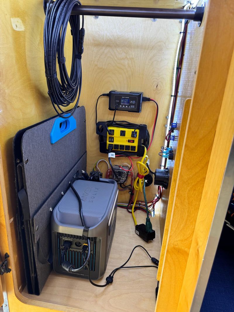 RV rental power setup in a wood cabinet, featuring an Anker Solix power station, smart charger, and stored solar panel. — photo 7