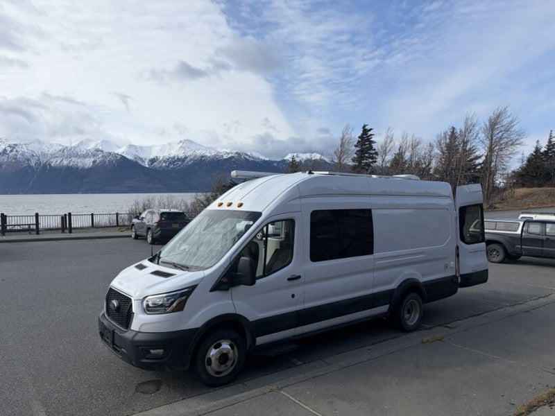  and stove looking out at scenic snowy mountains and water.|This inviting RV rental interior features an elevated bed — photo 7