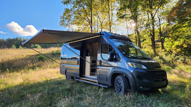 Enjoy nature with this RV rental! Dark grey camper van with awning extended in a sunny field. — photo 9