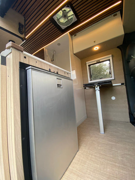 Sleek RV rental interior: large fridge, slatted wood ceiling w/ LED lights, fan, and fold-down table.