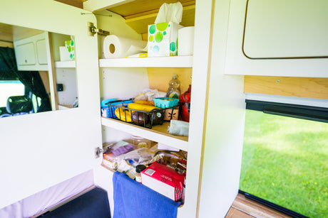 RV rental camper cabinet: organized storage with paper towels, tissues, fruit, and groceries. Mirror on the cabinet door.