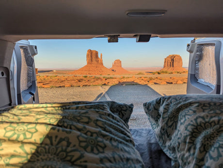 RV rental: Iconic Monument Valley red rock formations glow in golden light, viewed from inside a vehicle's bed.