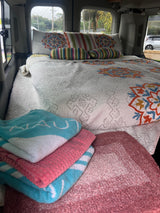 Cozy RV rental interior featuring a neatly made bed with colorful pillows, stacked towels, and a plush rug.