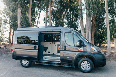 This gray Ram Promaster Tofino camper van RV rental shows its open side door and inviting interior setup, parked outdoors.