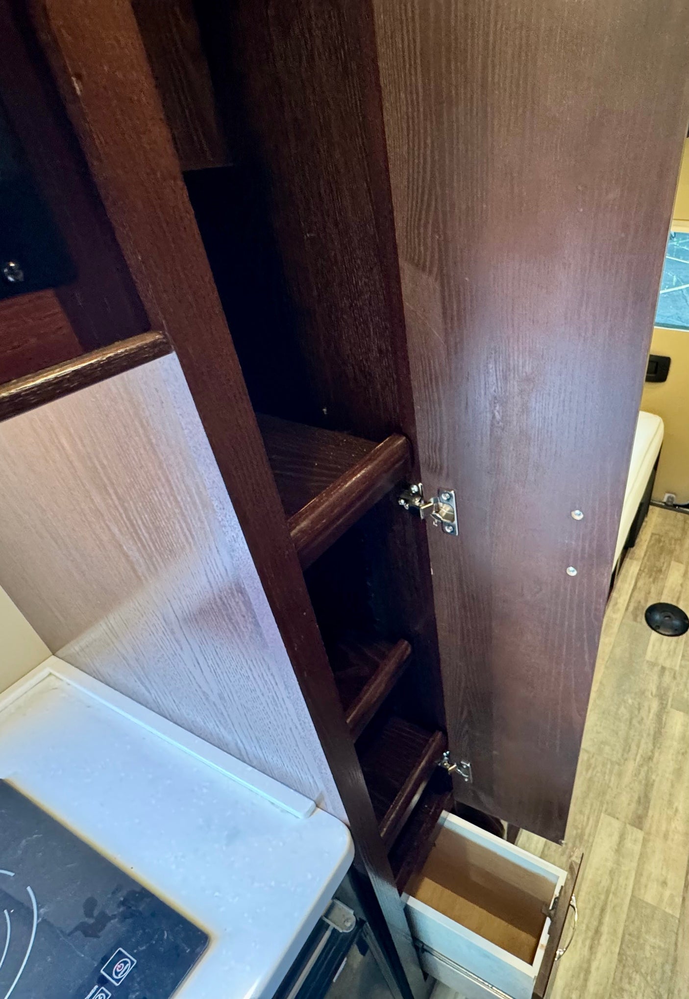 RV rental interior: Open dark wood cabinet with interior shelves, a pulled-out drawer, and a kitchen cooktop.