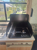 Functional RV rental kitchen with a gas stove, sink, and bright window offering an outdoor view.