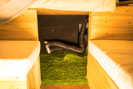 View between two light wood benches with cream cushions in an RV rental. A green astroturf floor and dark storage area are visible.