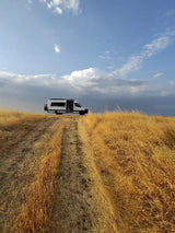 RV rental adventure! White camper van on a golden hill track under a partly cloudy blue sky, perfect for outdoor travel.