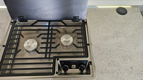 An RV rental kitchen features a Dometic 2-burner gas cooktop with open lid and integrated wireless phone charger.