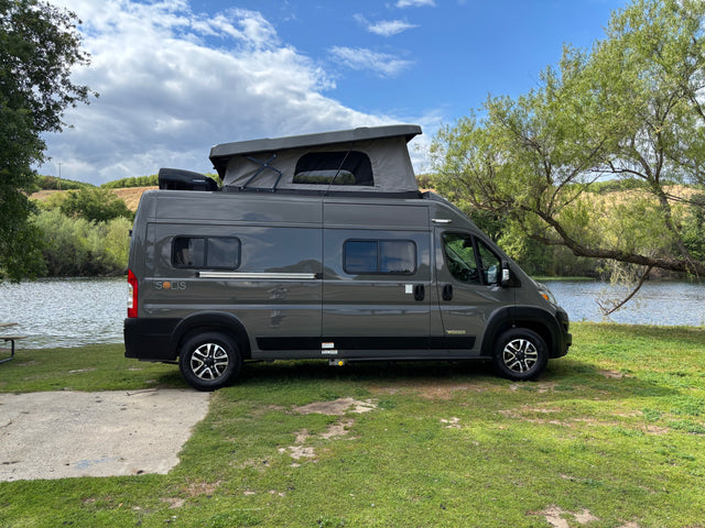 Gray Winnebago Solis RV rental parked by a lake. This camper van with a pop-top roof is on grass.