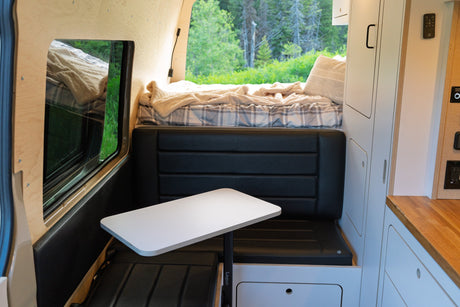 Cozy RV rental living space: bed, versatile table, and seating with a scenic forest view for your journey.