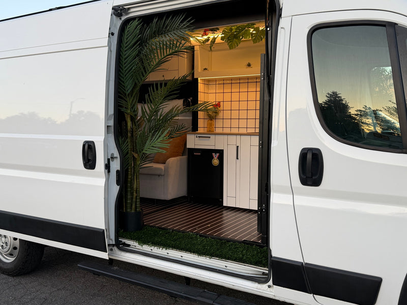 Stylish RV rental camper van interior with an open door, revealing a modern kitchen, seating, and vibrant plants. — photo 14