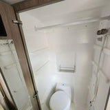 This RV rental features a clean, compact wet bath with a toilet, shower, and shelving, ideal for travel.