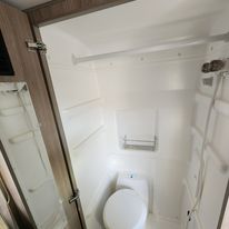 This RV rental features a clean, compact wet bath with a toilet, shower, and shelving, ideal for travel.