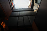 RV rental interior with a comfortable black leather bed/seating area, viewed from the front looking towards the open rear doors.