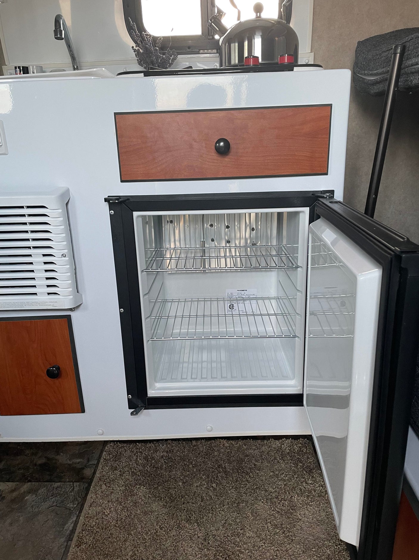 RV rental: Compact kitchenette with an open Dometic fridge, sink faucet, wood drawer, and AC vent.