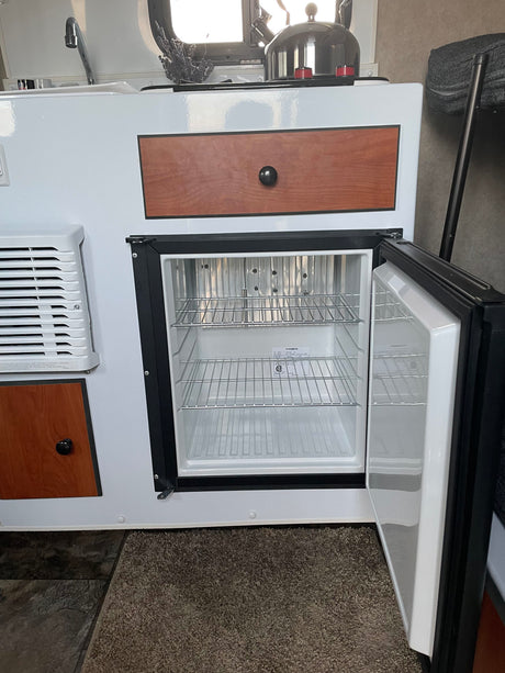 RV rental: Compact kitchenette with an open Dometic fridge, sink faucet, wood drawer, and AC vent.