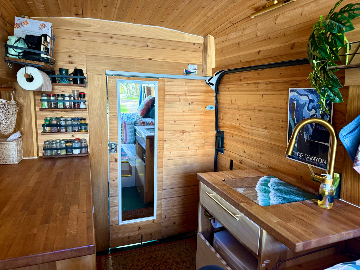 Inside this rv rental, a compact wooden kitchen with a sink, organized spice racks, and shelves create a cozy van interior.