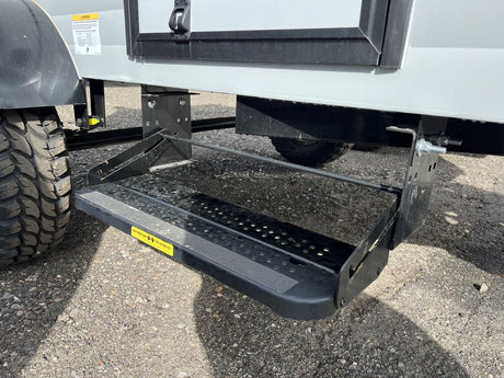 View of an RV rental's black, two-step pull-out entry system, with a rugged tire visible on the left.