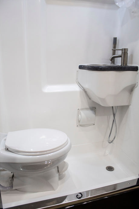 An RV rental compact bathroom with white toilet, sink, and shower. Space-saving design for comfortable mobile living.