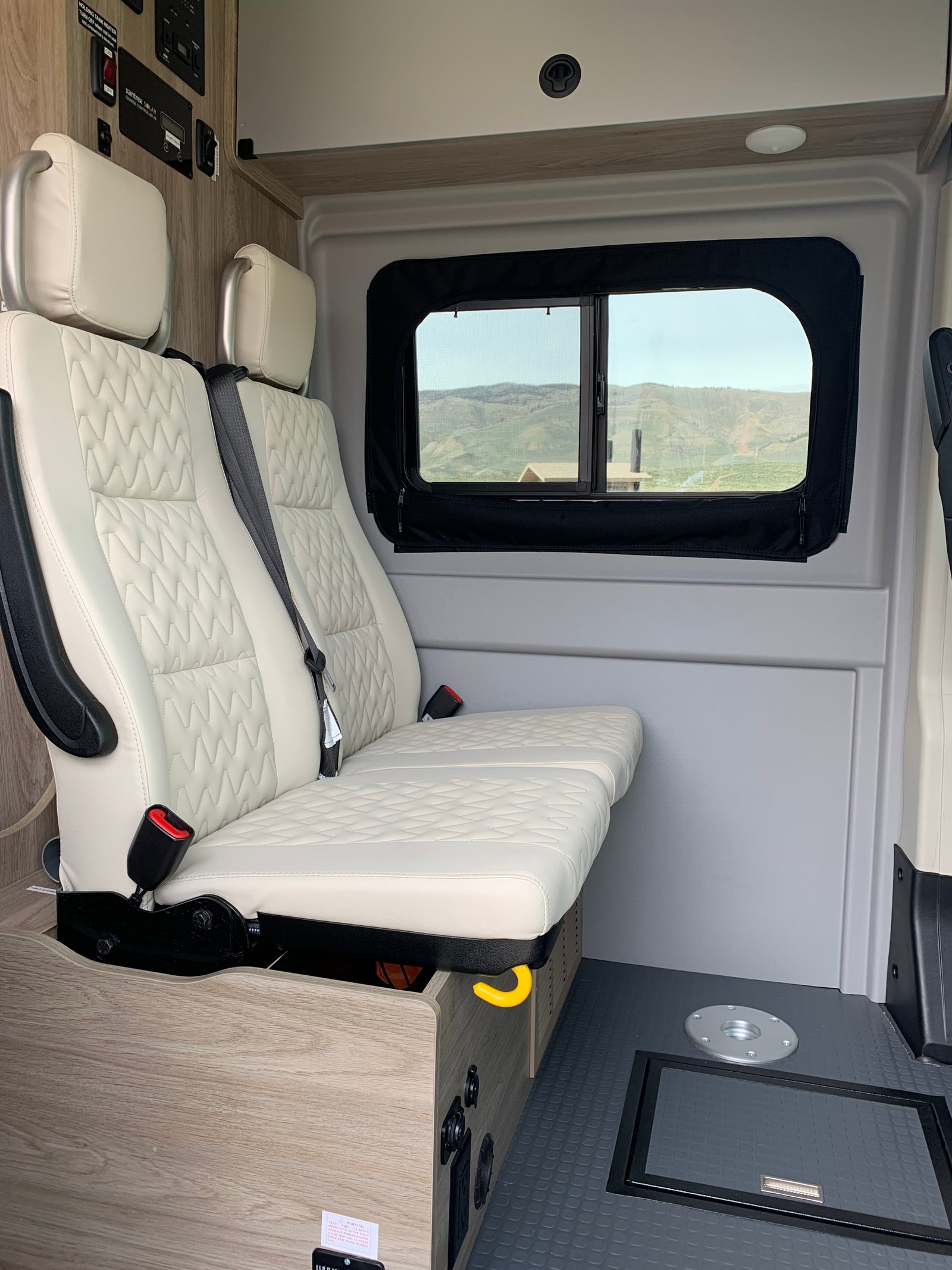 Inside an RV rental: cream passenger seats, a window with a scenic mountain view, and built-in solar control panels.
