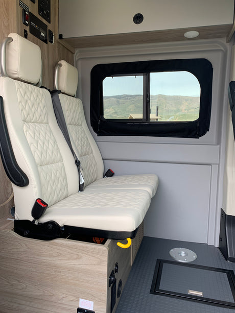 Inside an RV rental: cream passenger seats, a window with a scenic mountain view, and built-in solar control panels.