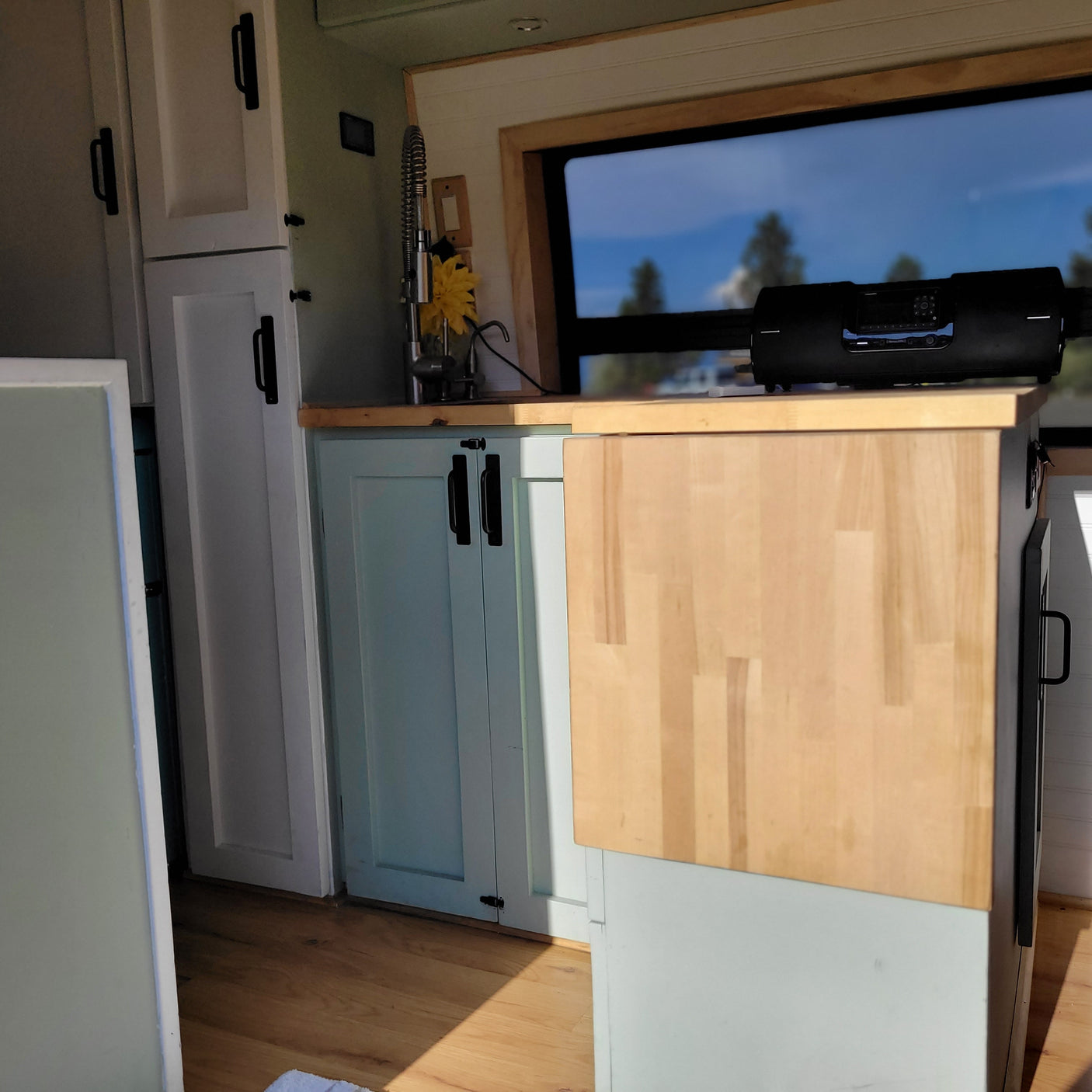 Experience comfort in this rv rental! Kitchen with light blue cabinets, wood counter, window view, and entertainment.