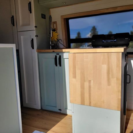 Experience comfort in this rv rental! Kitchen with light blue cabinets, wood counter, window view, and entertainment.