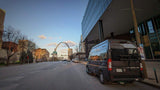 Black camper van RV rental parked on a city street with St. Louis's iconic Gateway Arch in the distance.