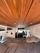 RV rental interior: warm wooden walls, white cabinets, cozy bed with laptop, and a compact kitchen.