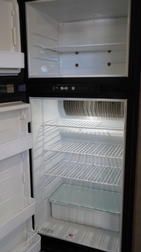 Clean, empty refrigerator and freezer interior, ideal for an RV rental. Features wire shelves and a crisper drawer.