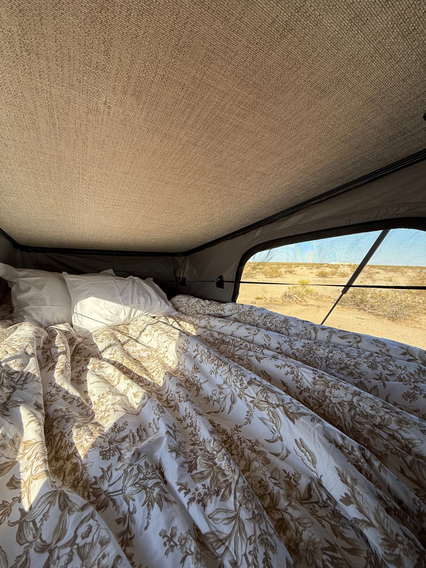Comfy bed in an rv rental rooftop tent, featuring a floral duvet and panoramic desert views. Ideal for glamping adventures.